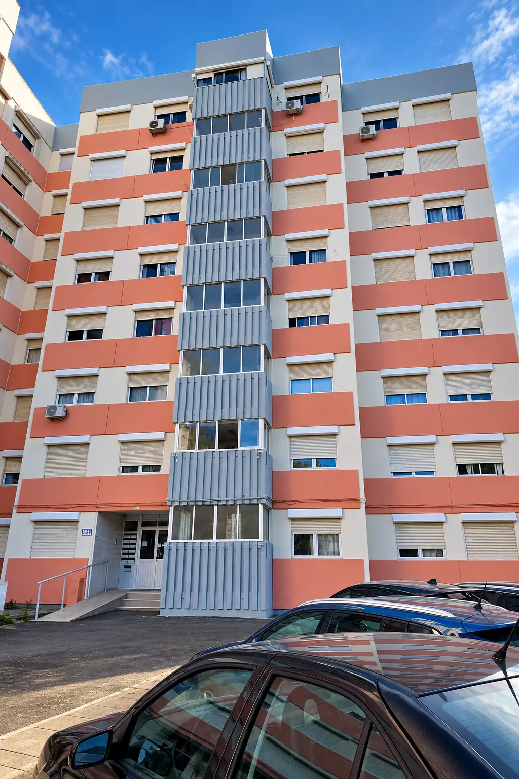 Fachada de prédio de habitação pintada em tons de laranja, branco e cinzento