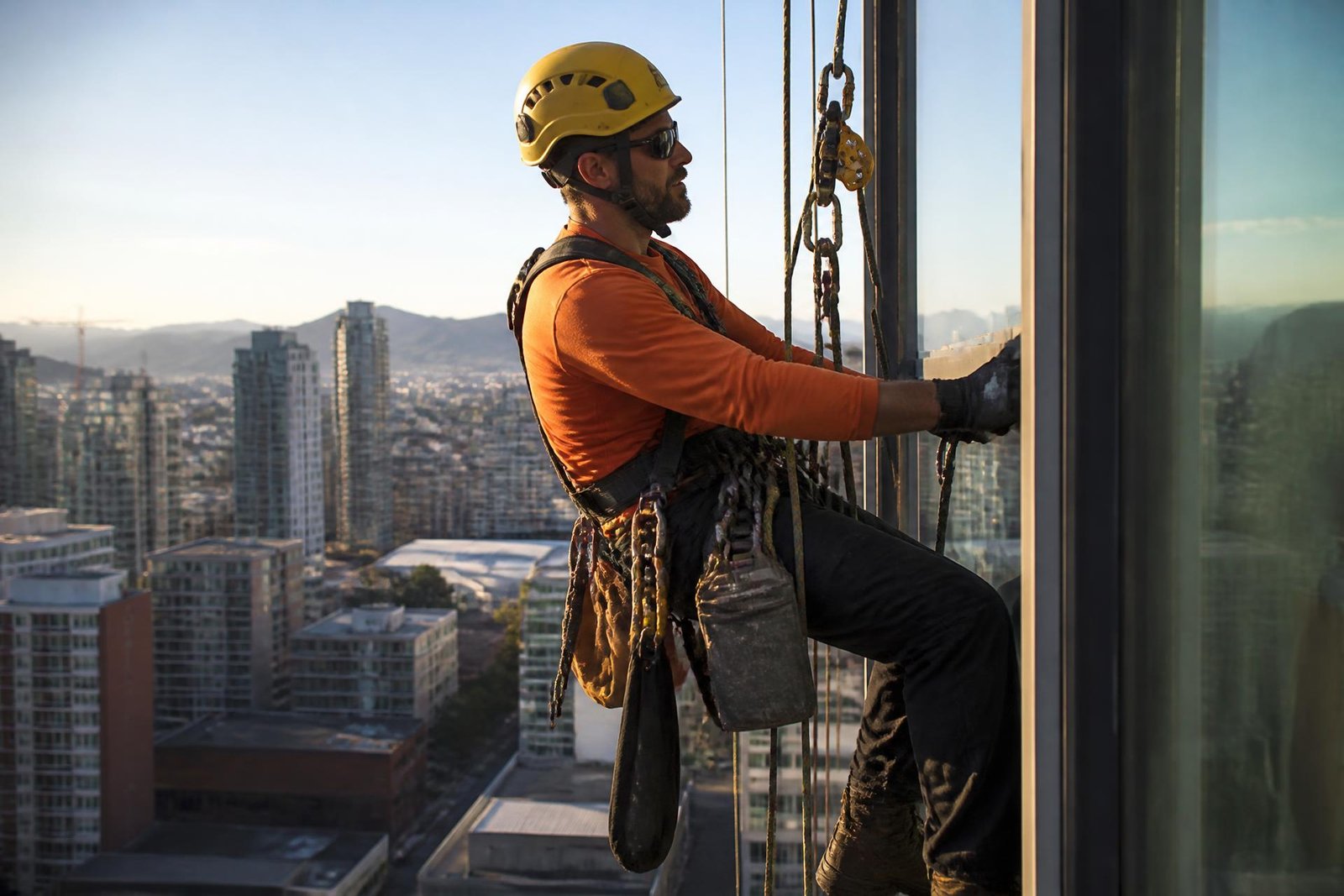 Técnico de acesso por cordas suspenso na fachada de um edifício alto ao fim da tarde